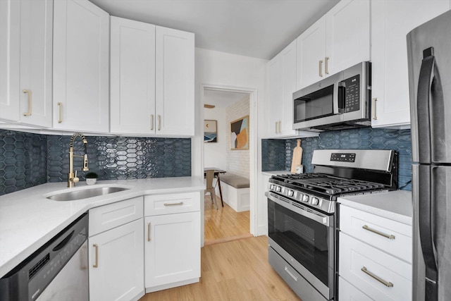 kitchen with light countertops, light wood-style flooring, stainless steel appliances, white cabinetry, and a sink