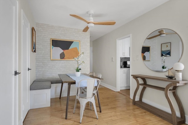 dining space featuring brick wall, light wood-style floors, and a ceiling fan