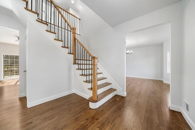 staircase featuring visible vents, a notable chandelier, wood finished floors, and baseboards