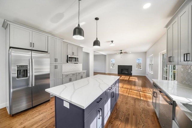 kitchen with gray cabinetry, wood finished floors, stainless steel appliances, decorative backsplash, and ceiling fan