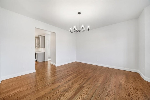 spare room featuring an inviting chandelier, wood finished floors, and baseboards