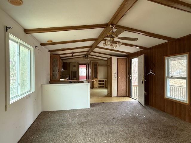 unfurnished living room featuring lofted ceiling with beams, wooden walls, ceiling fan, and carpet flooring