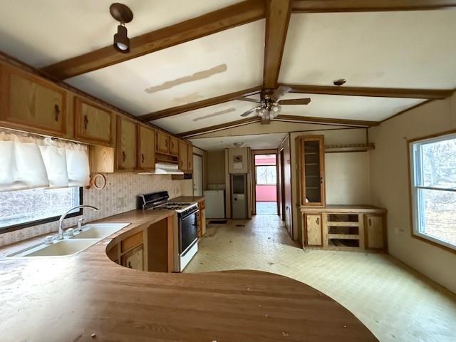 kitchen featuring vaulted ceiling with beams, a sink, under cabinet range hood, gas range, and brown cabinets