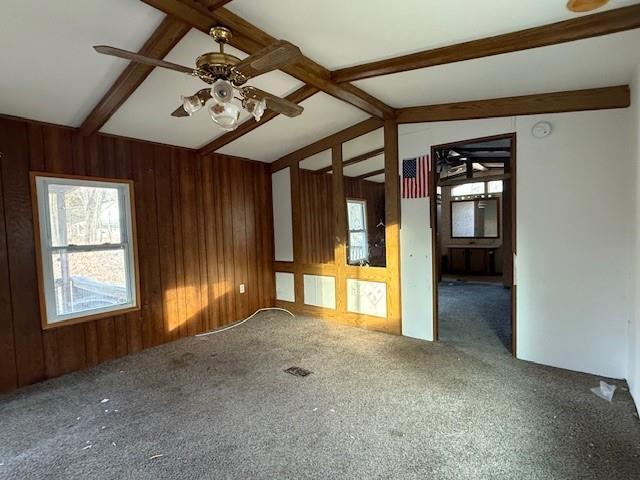 empty room featuring lofted ceiling with beams, wooden walls, carpet, and ceiling fan