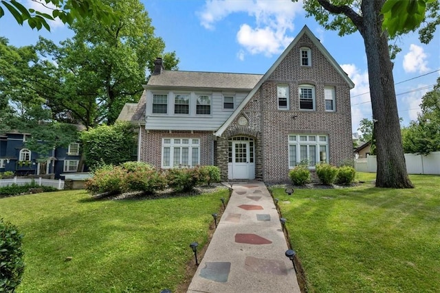 tudor home with brick siding, a chimney, a front lawn, and fence