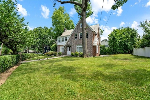 rear view of house with brick siding, fence, a lawn, and a chimney