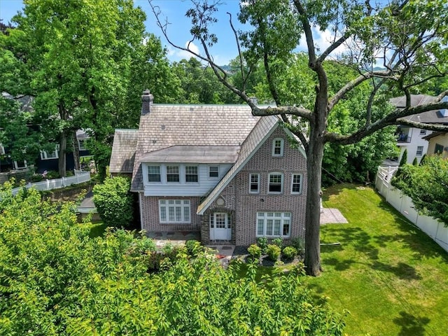 view of front of home featuring brick siding, a chimney, a front lawn, and fence