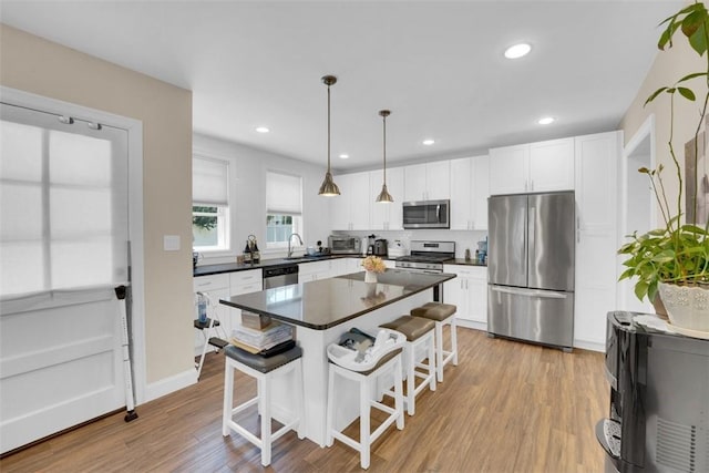 kitchen with a kitchen bar, light wood-style flooring, dark countertops, stainless steel appliances, and white cabinets