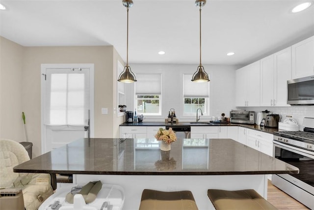 kitchen featuring a sink, a kitchen breakfast bar, backsplash, white cabinetry, and appliances with stainless steel finishes