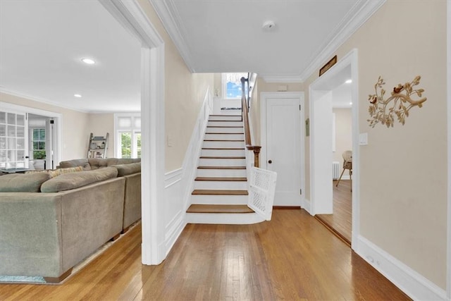 staircase featuring wood finished floors, radiator heating unit, recessed lighting, ornamental molding, and wainscoting