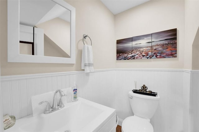 half bath featuring a sink, toilet, and wainscoting