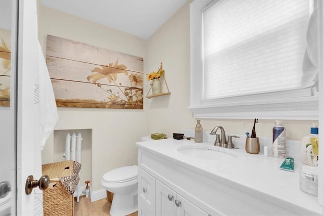 half bathroom with toilet, vanity, baseboards, and wood finished floors