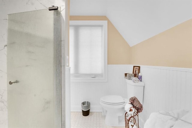 bathroom with a shower stall, toilet, a wainscoted wall, and vaulted ceiling