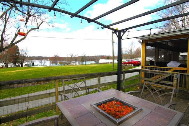 wooden terrace with a lawn, a fire pit, fence, and a water view