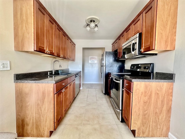 kitchen featuring light tile patterned floors, baseboards, a sink, stainless steel appliances, and dark countertops