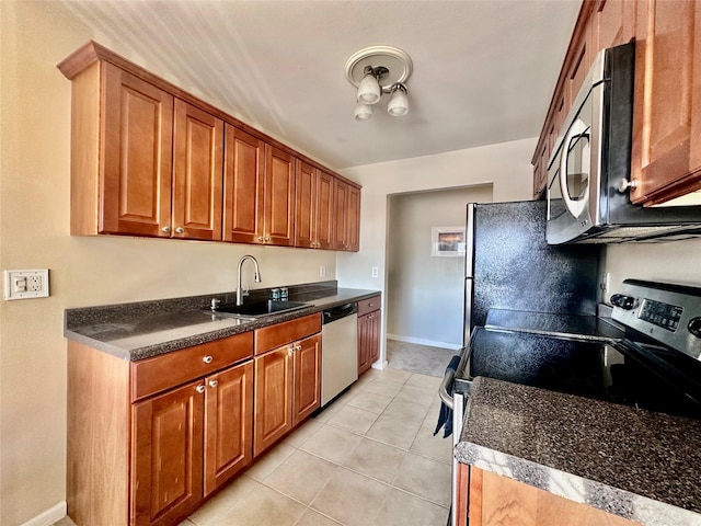 kitchen featuring brown cabinets, a sink, dark countertops, stainless steel appliances, and light tile patterned floors