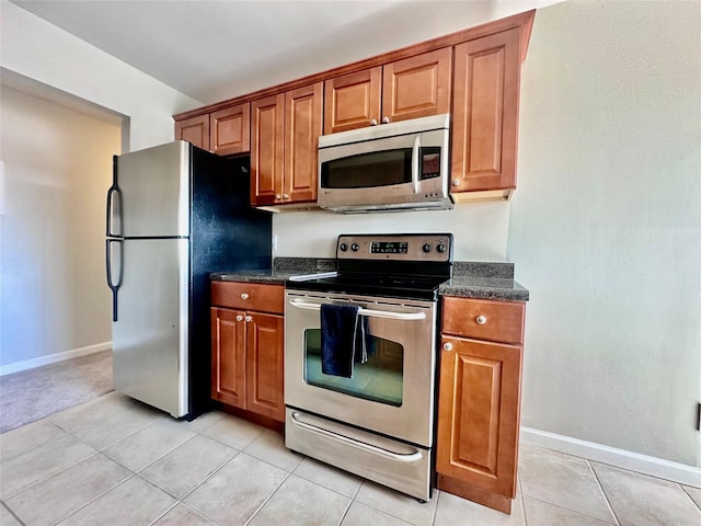 kitchen with light tile patterned flooring, baseboards, brown cabinets, and appliances with stainless steel finishes