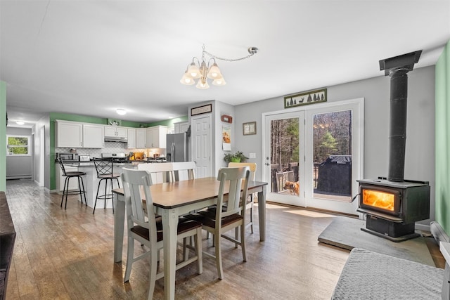 dining room with plenty of natural light, a wood stove, light wood finished floors, and an inviting chandelier