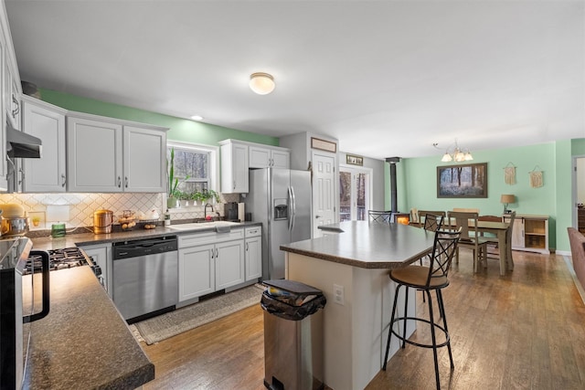 kitchen with dark countertops, a notable chandelier, appliances with stainless steel finishes, a kitchen bar, and backsplash