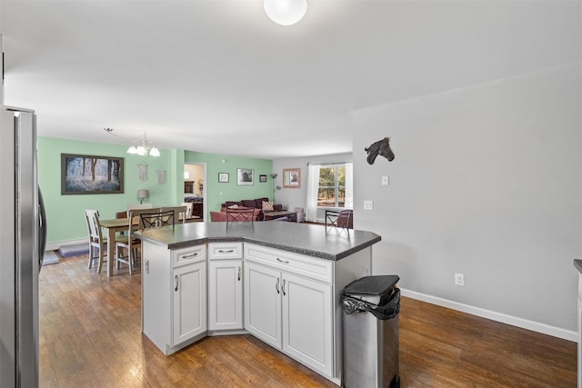 kitchen with dark countertops, wood finished floors, white cabinets, freestanding refrigerator, and an inviting chandelier