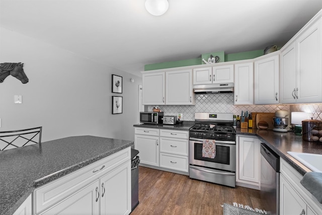 kitchen with decorative backsplash, dark countertops, under cabinet range hood, white cabinets, and appliances with stainless steel finishes