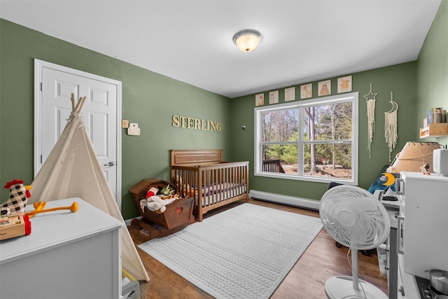 bedroom featuring a nursery area, a baseboard heating unit, and wood finished floors