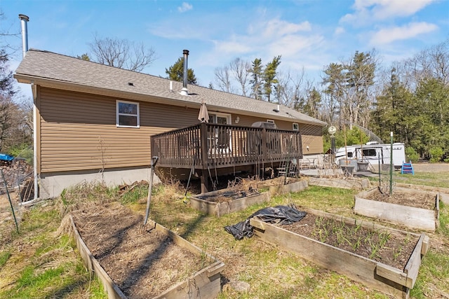 back of property with roof with shingles, a wooden deck, and a garden