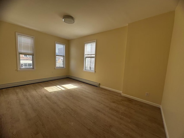 empty room with a baseboard radiator, baseboards, and wood finished floors