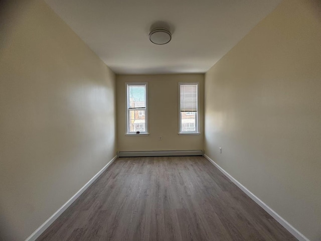 spare room featuring a baseboard heating unit, baseboards, and dark wood-type flooring