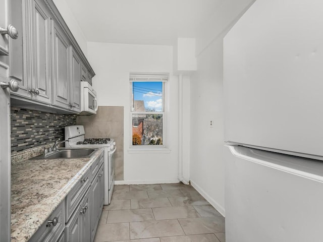 kitchen featuring gray cabinets, a sink, white appliances, decorative backsplash, and baseboards