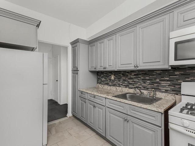 kitchen with a sink, white appliances, gray cabinetry, and light countertops