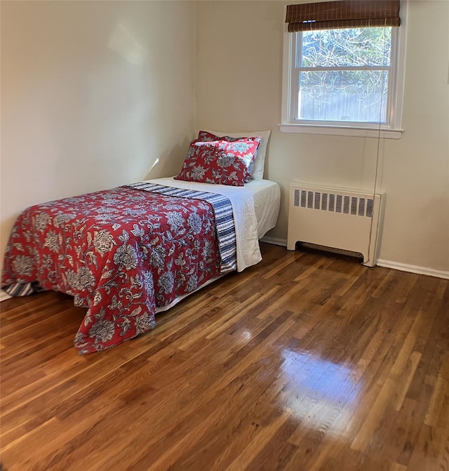 bedroom with radiator heating unit, wood finished floors, and baseboards