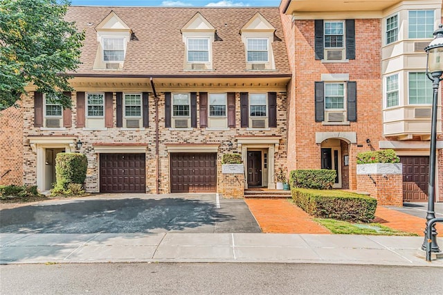 multi unit property featuring brick siding, an attached garage, roof with shingles, and driveway