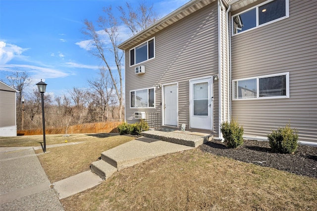 view of front of home with a wall mounted air conditioner and a front yard