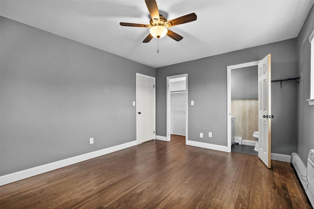 unfurnished bedroom featuring a walk in closet, dark wood-type flooring, baseboards, baseboard heating, and ensuite bath