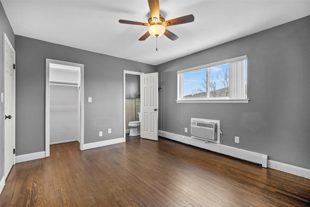 unfurnished bedroom featuring baseboards, an AC wall unit, hardwood / wood-style floors, ensuite bathroom, and a baseboard radiator