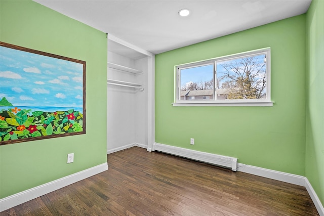 unfurnished bedroom with a closet, baseboard heating, baseboards, and wood finished floors