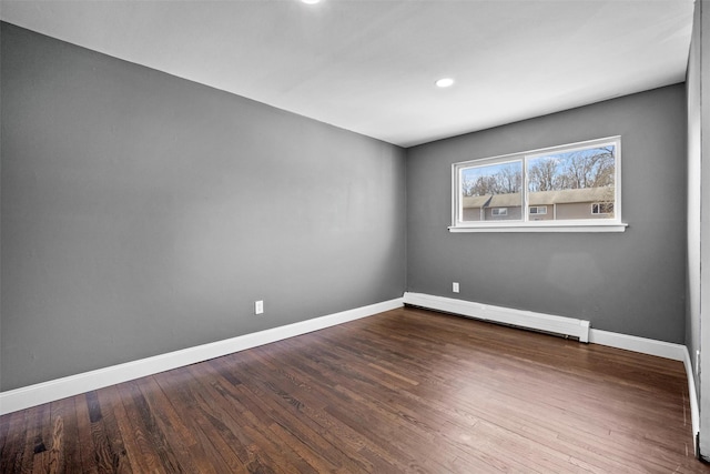 spare room featuring a baseboard heating unit, baseboards, and wood finished floors