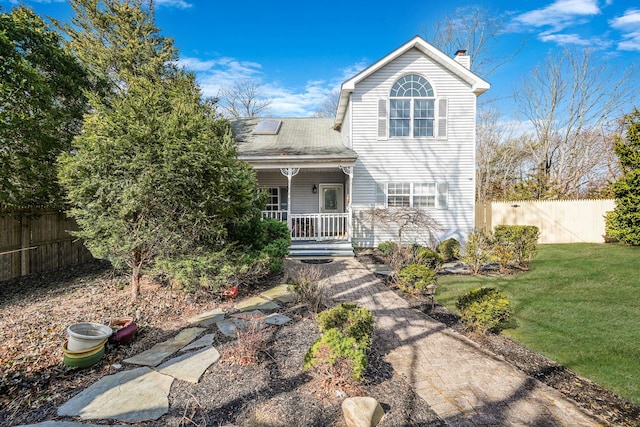 traditional-style home with fence, a porch, roof with shingles, a front yard, and a chimney