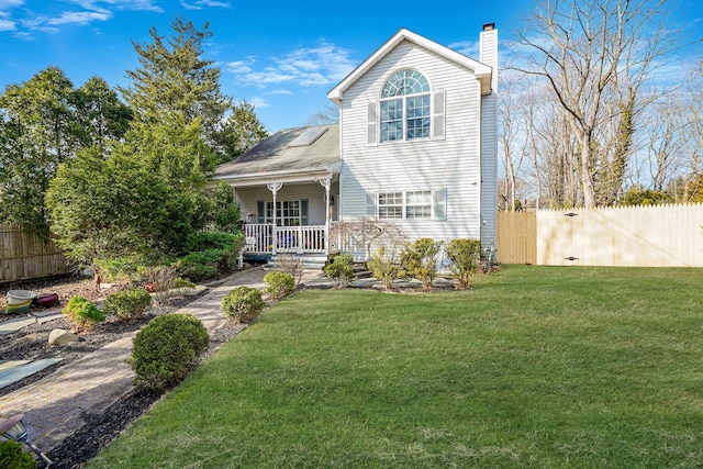 view of front of home featuring a chimney, covered porch, a front yard, and fence