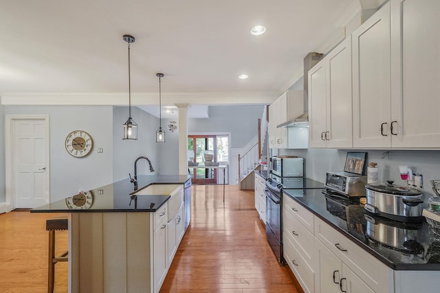 kitchen featuring electric range, a breakfast bar, light wood-style flooring, a sink, and wall chimney exhaust hood