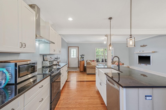 kitchen with open floor plan, appliances with stainless steel finishes, light wood-style floors, wall chimney exhaust hood, and a sink