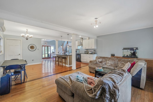 living room featuring baseboards, a notable chandelier, ornamental molding, and light wood finished floors