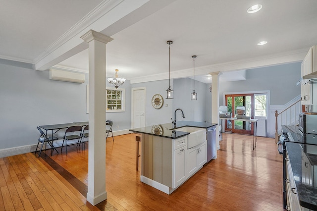 kitchen featuring a sink, dark countertops, stainless steel dishwasher, white cabinets, and decorative columns