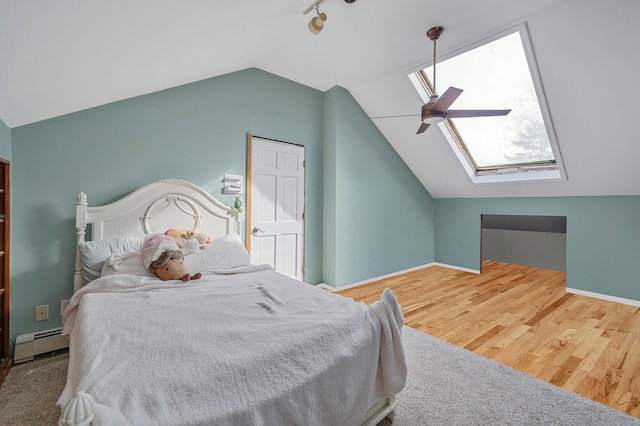 bedroom with lofted ceiling with skylight, a ceiling fan, a baseboard heating unit, wood finished floors, and baseboards