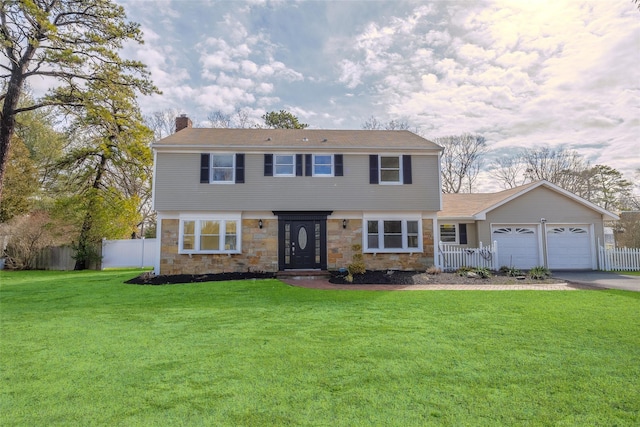 colonial home with fence, an attached garage, a chimney, a front lawn, and stone siding