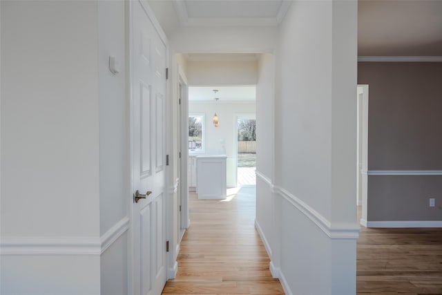 hallway with baseboards, light wood finished floors, and ornamental molding