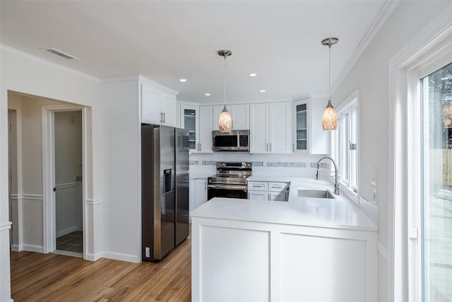 kitchen with a peninsula, a sink, stainless steel appliances, glass insert cabinets, and crown molding