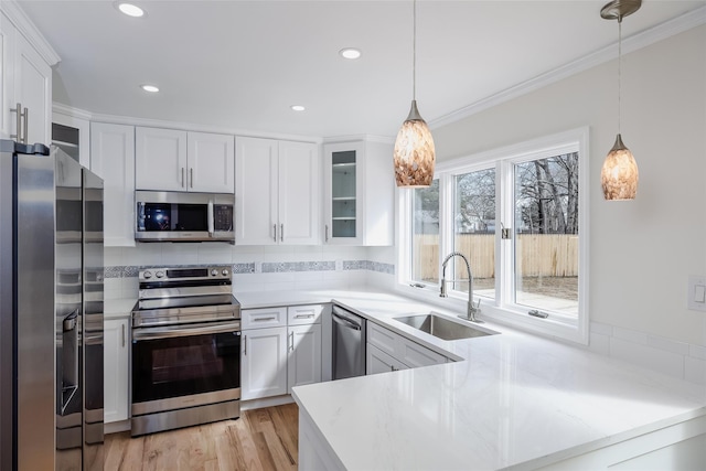 kitchen featuring a peninsula, ornamental molding, a sink, appliances with stainless steel finishes, and white cabinetry