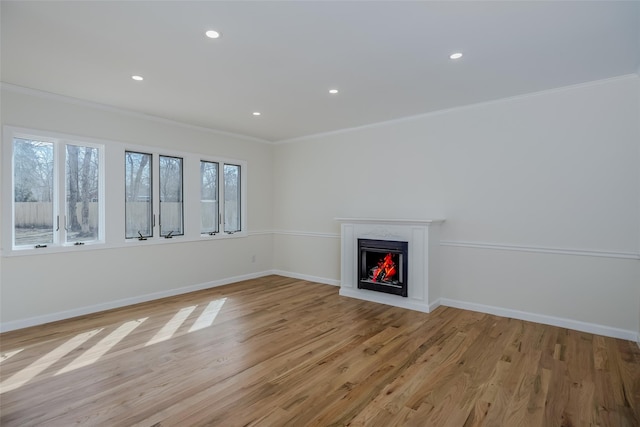 unfurnished living room featuring baseboards, light wood finished floors, recessed lighting, a warm lit fireplace, and crown molding